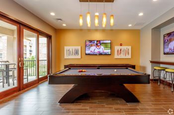 A pool table in a room with a television and bar stools.